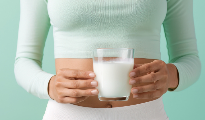 Laktoseintoleranz Frau mit türkisem Obereil und weissen Hosen haelt mit beiden Haenden ein Glas Milch.