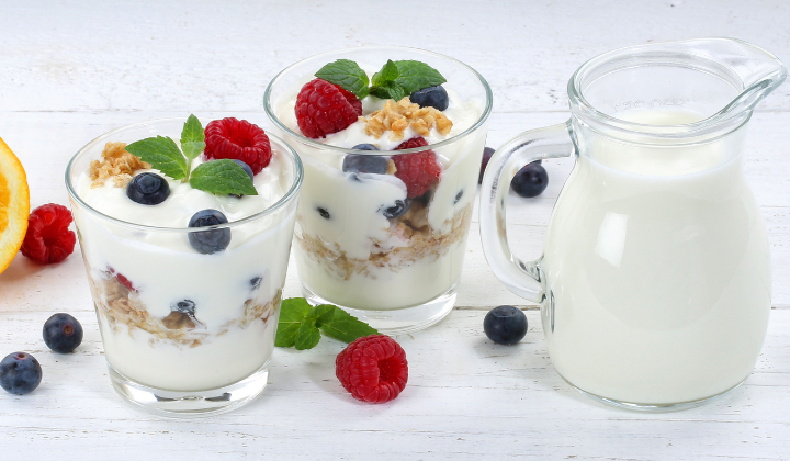Verzicht auf Milchprodukte Zwei Gläser geschichtet mit Yoghurt, Muesli, Blaubeeren, Himbeeren. Daneben steht eine Milchkannchen aus Glas.